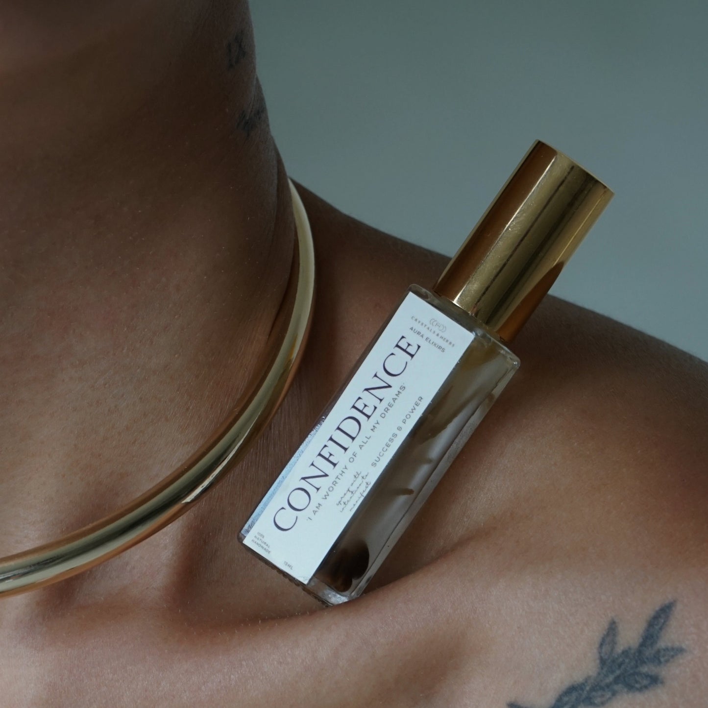 Close-up of a person wearing a gold necklace with a 'Confidence' perfume bottle